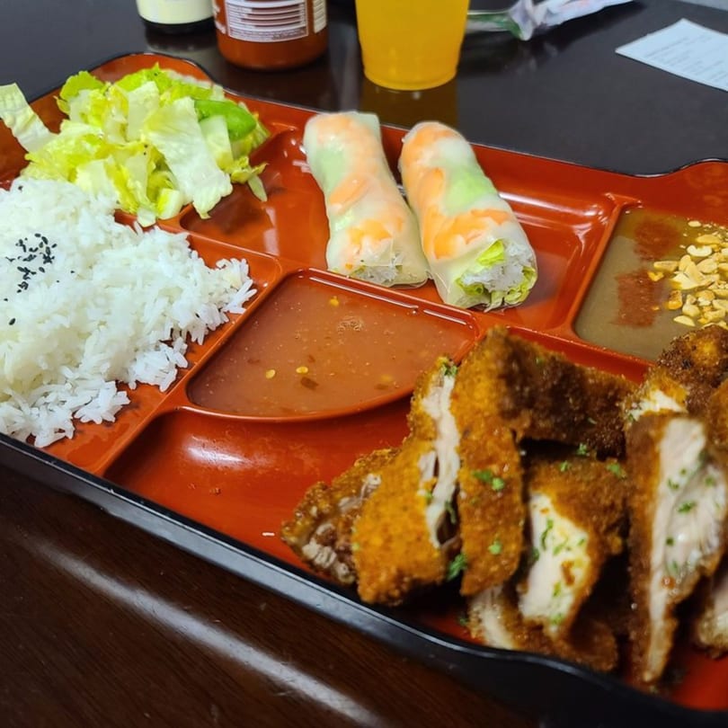 Saigon Bento's Vietnamese bento box with fried chicken, rice, lettuce, spring rolls, and sauces.