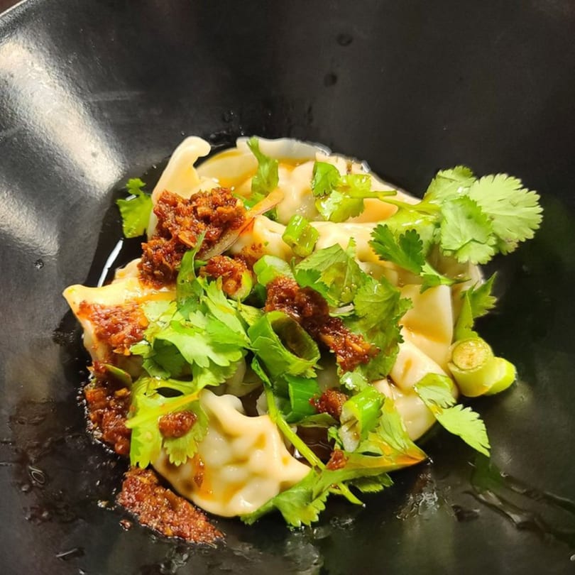 Vietnamese dumplings topped with chili oil, fresh cilantro, and green onions in a black bowl.