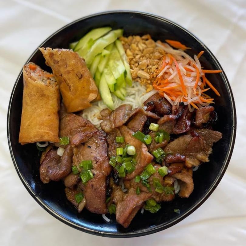 A Vietnamese Saigon Bento bowl with grilled pork, spring rolls, noodles, vegetables, and peanuts.