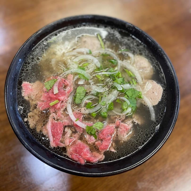 A bowl of Vietnamese pho with rare beef, meatballs, onions, and cilantro in broth.