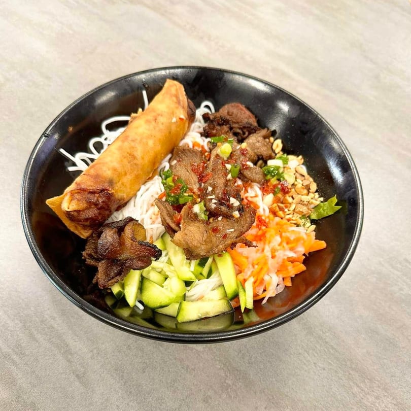 A Vietnamese vermicelli bowl with grilled pork, a crispy spring roll, and fresh vegetables.