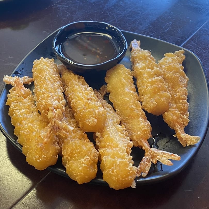Golden fried shrimp tempura with a side of dipping sauce on a black plate.